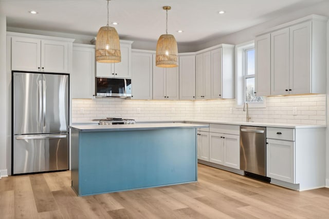 kitchen with stainless steel appliances, hanging light fixtures, white cabinets, and light hardwood / wood-style flooring