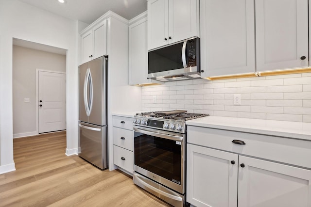 kitchen with light stone counters, light hardwood / wood-style flooring, appliances with stainless steel finishes, decorative backsplash, and white cabinets