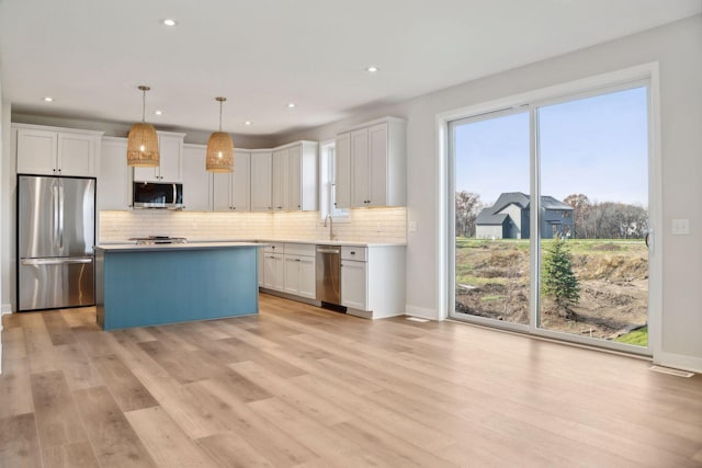 kitchen with white cabinetry, appliances with stainless steel finishes, hanging light fixtures, and light wood-type flooring