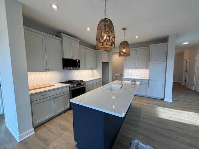 kitchen with pendant lighting, sink, decorative backsplash, a kitchen island with sink, and gas stove