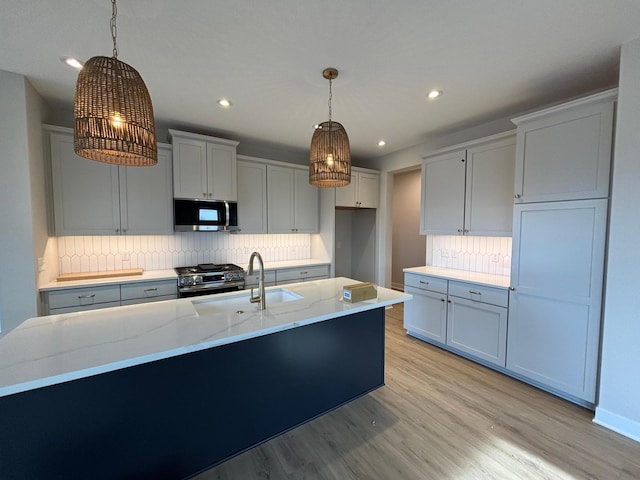 kitchen featuring sink, appliances with stainless steel finishes, light stone counters, a center island with sink, and decorative light fixtures