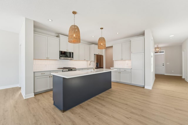 kitchen with backsplash, hanging light fixtures, light hardwood / wood-style floors, stainless steel appliances, and a center island with sink