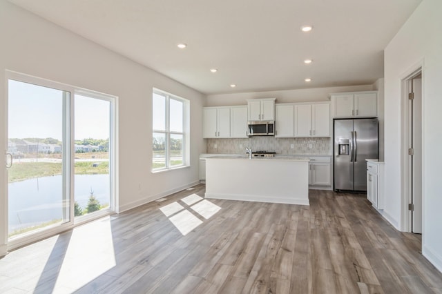 kitchen with appliances with stainless steel finishes, white cabinetry, decorative backsplash, light hardwood / wood-style flooring, and a center island with sink