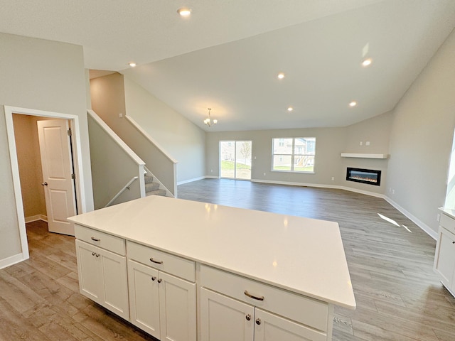 kitchen featuring white cabinets, vaulted ceiling, a kitchen island, and light wood-type flooring