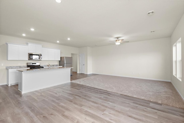 kitchen with white cabinets, stainless steel appliances, a kitchen island with sink, light wood-type flooring, and ceiling fan