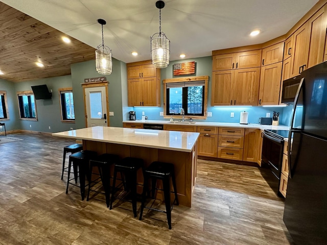 kitchen featuring a kitchen bar, sink, decorative light fixtures, a kitchen island, and black appliances