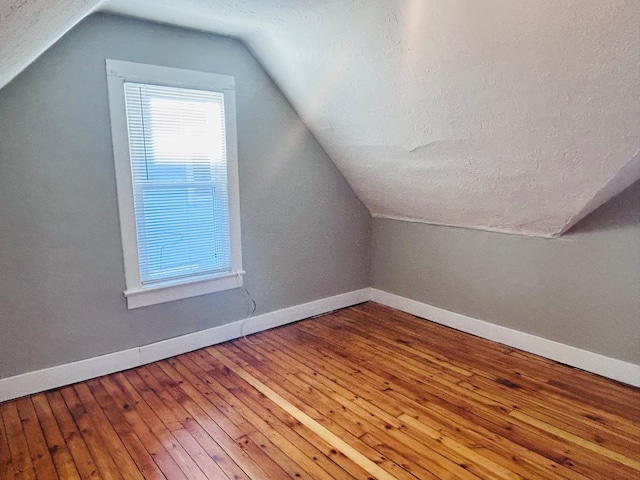 additional living space featuring lofted ceiling, hardwood / wood-style floors, and a textured ceiling