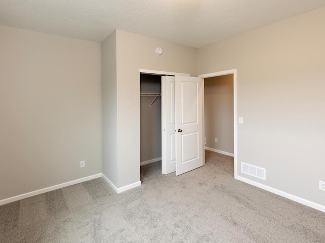 unfurnished bedroom with light colored carpet, a textured ceiling, and a closet