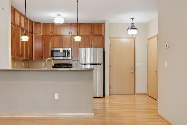 kitchen with hanging light fixtures, stainless steel appliances, kitchen peninsula, and light wood-type flooring