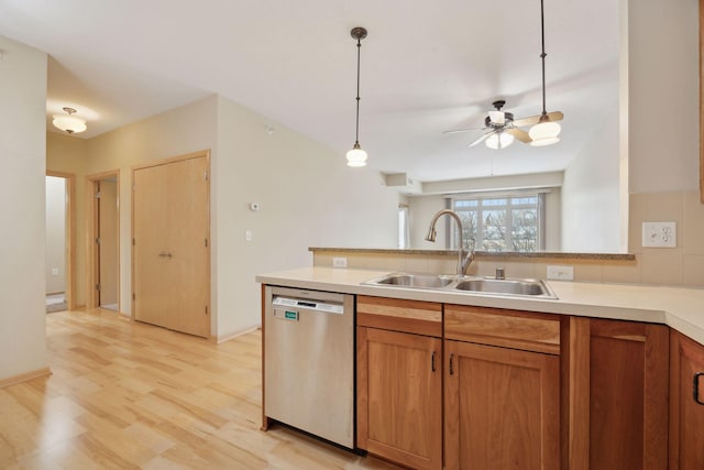 kitchen featuring light countertops, hanging light fixtures, stainless steel dishwasher, brown cabinetry, and a sink