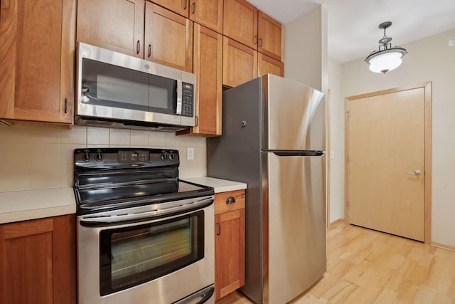 kitchen featuring stainless steel appliances, light countertops, hanging light fixtures, and backsplash