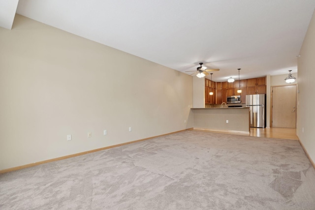 unfurnished living room featuring a ceiling fan, light colored carpet, and baseboards