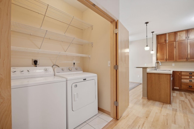 laundry room featuring washer and clothes dryer, light wood-style floors, a sink, laundry area, and baseboards