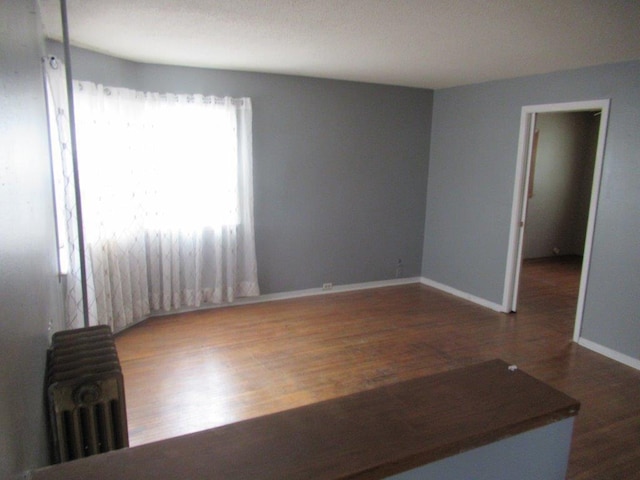 unfurnished room with dark wood-type flooring and radiator heating unit