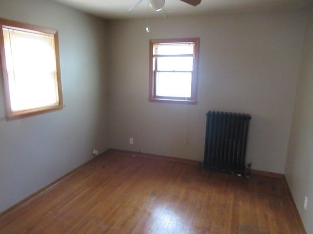 unfurnished room featuring ceiling fan, hardwood / wood-style floors, and radiator heating unit