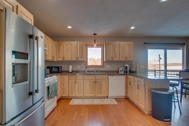 kitchen featuring kitchen peninsula, light brown cabinetry, white appliances, and decorative light fixtures