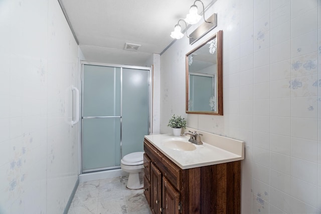 bathroom featuring vanity, a shower with shower door, tile walls, and toilet