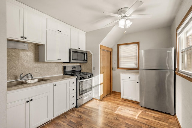 kitchen featuring appliances with stainless steel finishes, sink, white cabinets, decorative backsplash, and light hardwood / wood-style floors