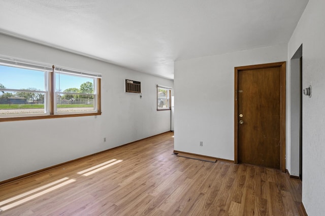 spare room with light wood-style flooring, a wall unit AC, and baseboards
