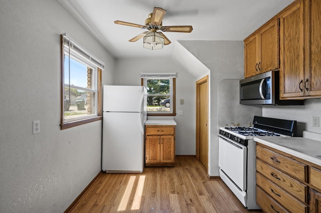 kitchen with freestanding refrigerator, gas range oven, stainless steel microwave, and brown cabinetry