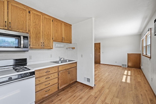 kitchen featuring white gas stove, stainless steel microwave, light wood-style floors, a sink, and light countertops