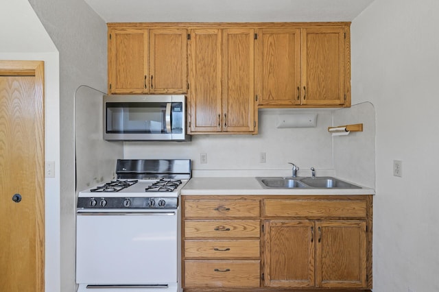 kitchen featuring stainless steel microwave, gas range gas stove, a sink, light countertops, and brown cabinetry