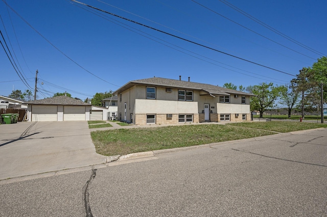 raised ranch with a detached garage, an outdoor structure, brick siding, a front yard, and stucco siding