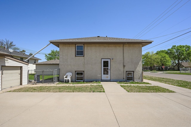 rear view of property featuring stucco siding, fence, and a gate