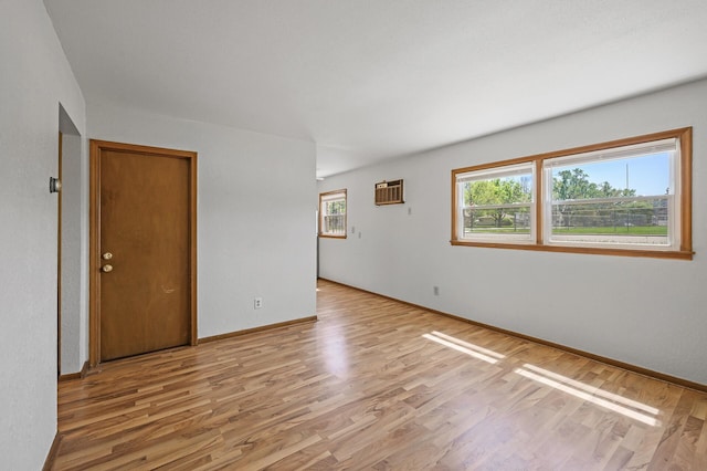 unfurnished room featuring light wood-style floors, baseboards, and an AC wall unit