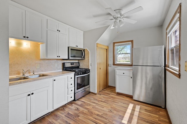 kitchen featuring stainless steel appliances, a sink, light wood-type flooring, a ceiling fan, and white cabinets