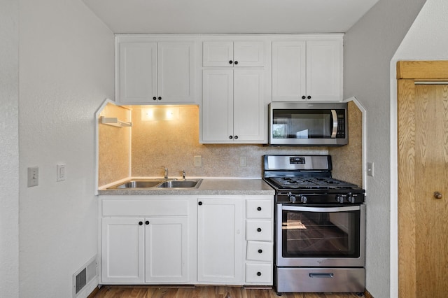 kitchen with stainless steel appliances, a sink, white cabinets, light countertops, and decorative backsplash