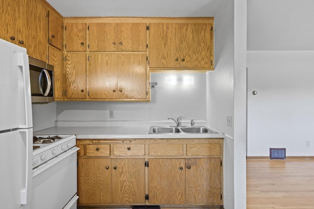 kitchen with white appliances, a sink, light countertops, and wood finished floors