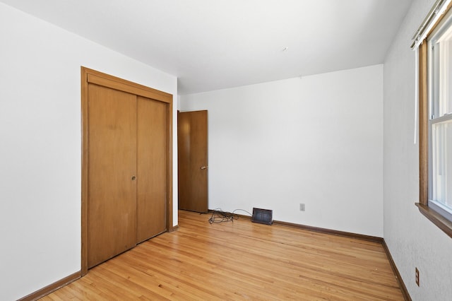 unfurnished bedroom featuring light wood-type flooring, a closet, and baseboards