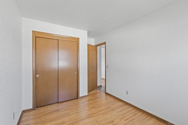 unfurnished bedroom featuring light wood finished floors, baseboards, and a closet