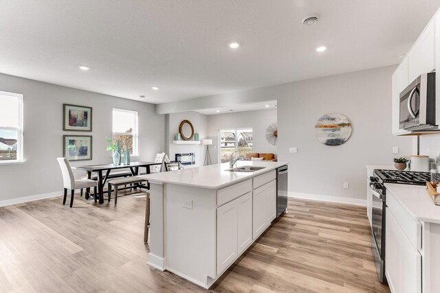 kitchen featuring appliances with stainless steel finishes, a wealth of natural light, white cabinetry, sink, and a kitchen island with sink