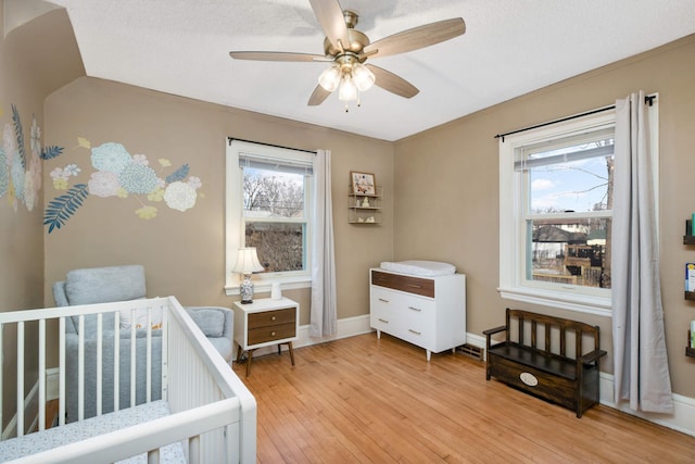 bedroom with multiple windows, ceiling fan, a crib, and light wood-type flooring