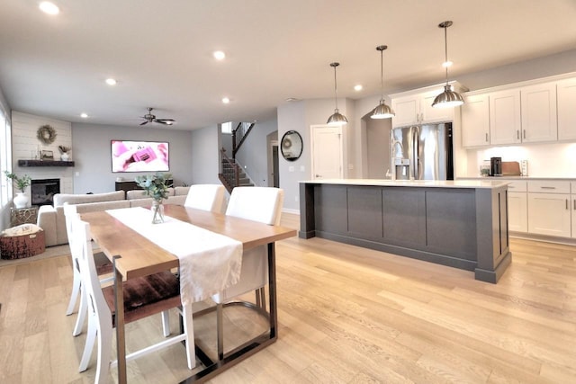 dining space with ceiling fan, a large fireplace, and light wood-type flooring