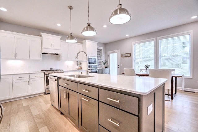 kitchen with decorative light fixtures, white cabinetry, an island with sink, sink, and stainless steel appliances