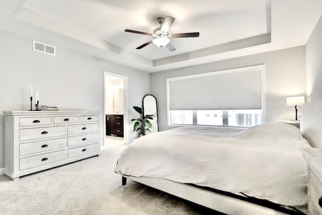 carpeted bedroom featuring a tray ceiling, a textured ceiling, ceiling fan, and ensuite bathroom