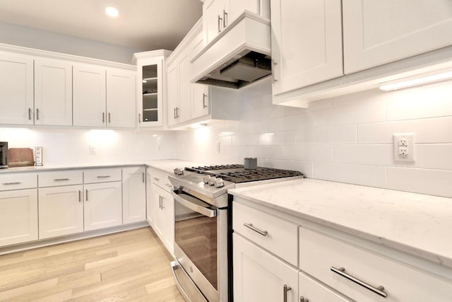 kitchen featuring tasteful backsplash, light stone countertops, white cabinets, stainless steel range with gas cooktop, and custom exhaust hood