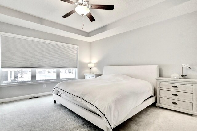 carpeted bedroom featuring a raised ceiling and ceiling fan