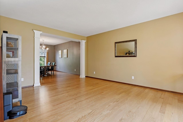 spare room with a notable chandelier, light hardwood / wood-style floors, and ornate columns