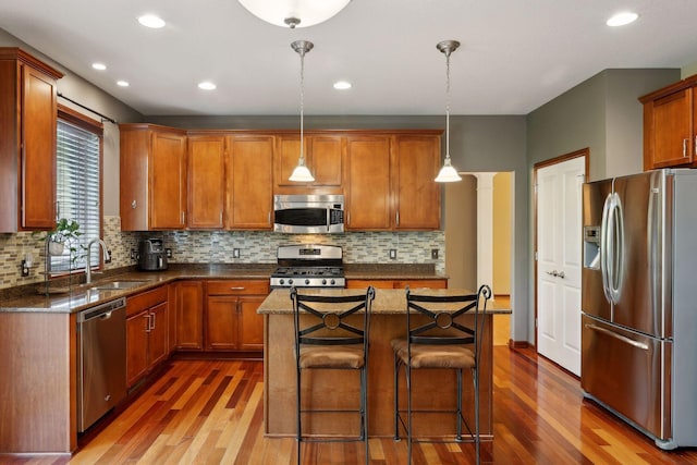 kitchen featuring a kitchen island, appliances with stainless steel finishes, pendant lighting, a breakfast bar, and dark wood-type flooring