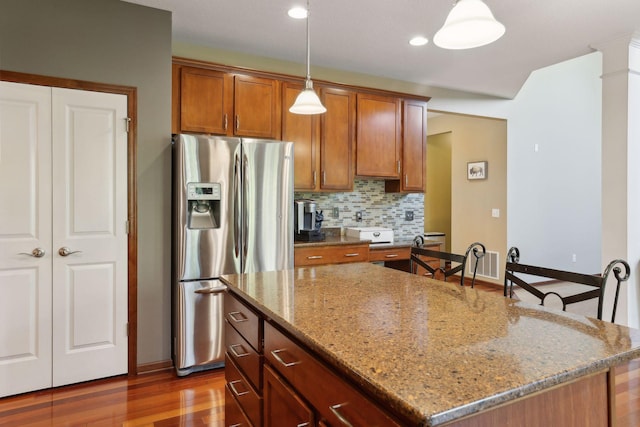 kitchen with a center island, stainless steel fridge, pendant lighting, light stone countertops, and decorative backsplash