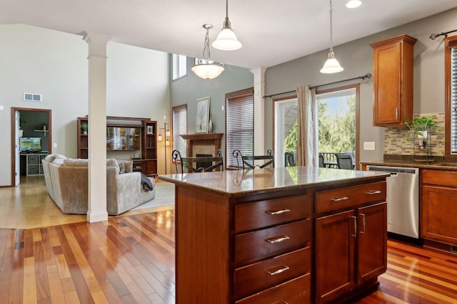 kitchen with hanging light fixtures, tasteful backsplash, a kitchen island, stainless steel dishwasher, and ornate columns