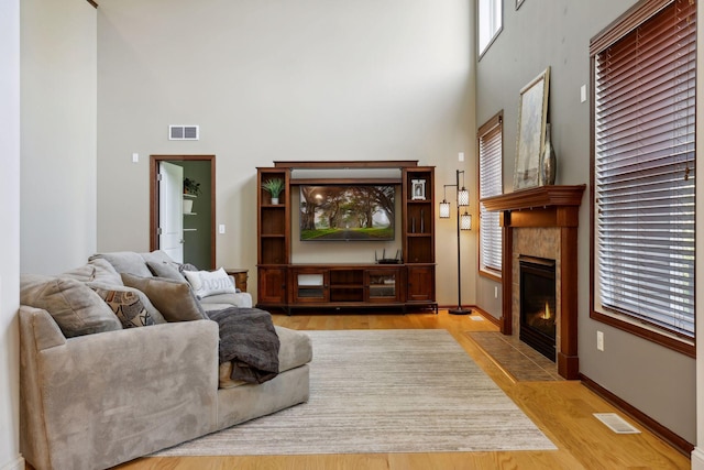 living room with a towering ceiling, a tiled fireplace, and light wood-type flooring