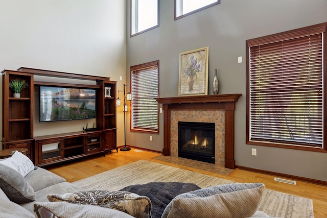 living room featuring a towering ceiling, light hardwood / wood-style floors, and a tile fireplace