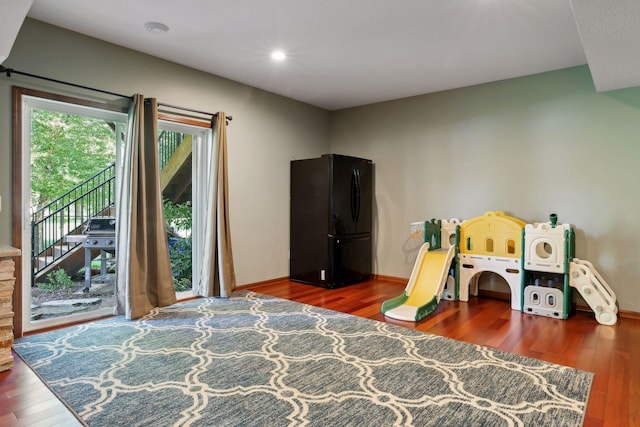 bedroom featuring access to exterior, dark hardwood / wood-style floors, and black fridge