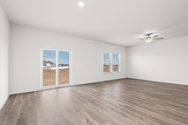 spare room with a healthy amount of sunlight, ceiling fan, baseboards, and wood finished floors