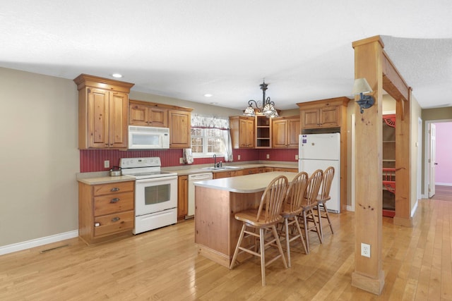 kitchen featuring white appliances, a sink, a kitchen island, light countertops, and brown cabinetry